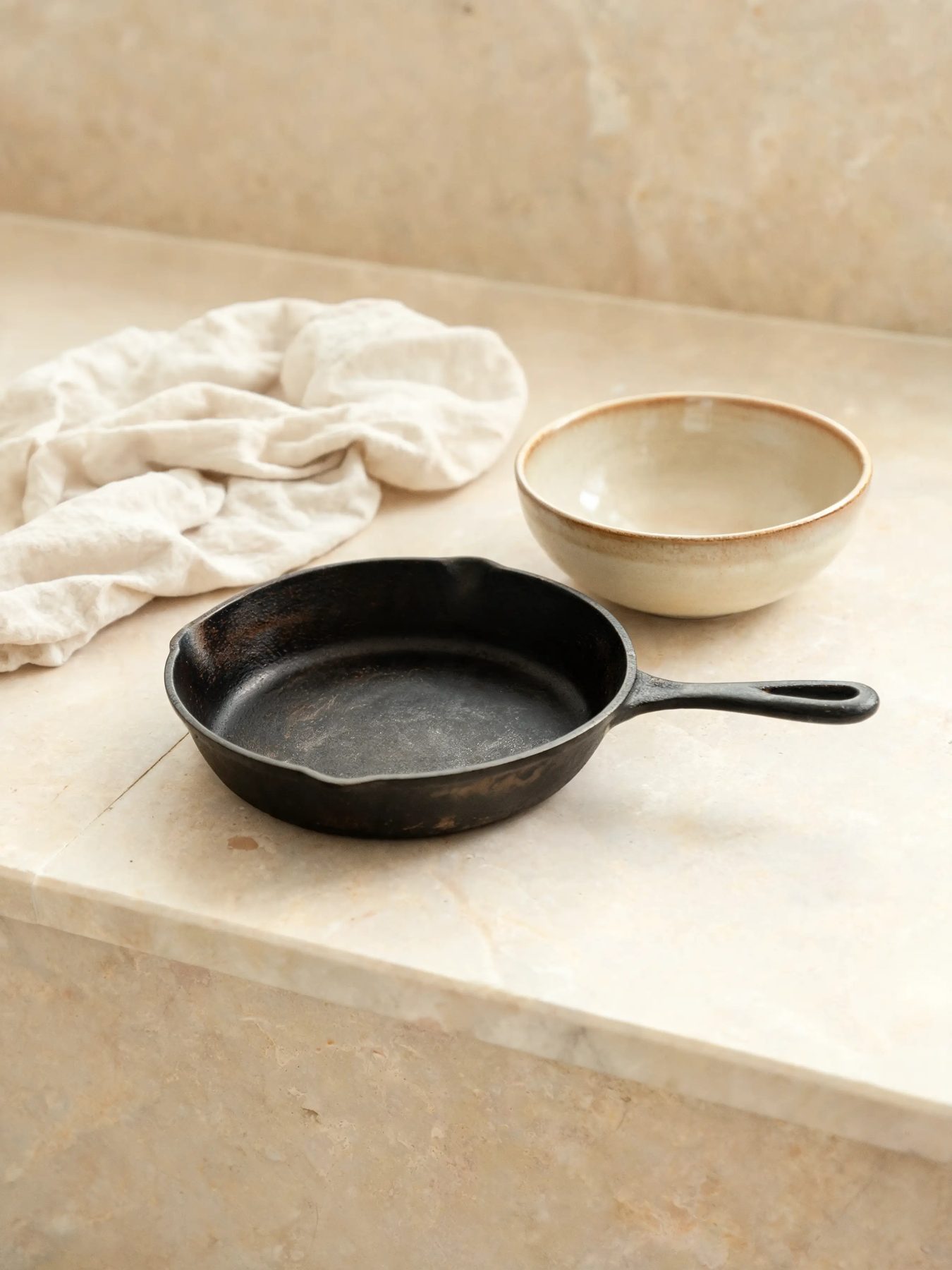 Seasoned skillet and glazed stoneware bowl on a limestone counter